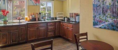 Una cocina con armarios de madera, una mesa de comedor y sillas. Se ve una ventana con vistas al exterior.