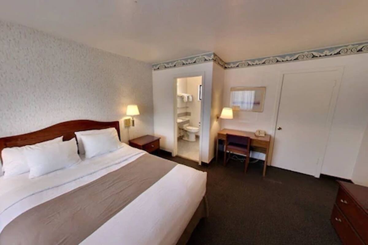 A hotel room with a bed, bedside tables, a desk, a chair, a wardrobe, and a bathroom with a toilet and sink.