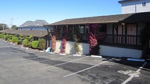A motel with a parking lot, a covered outdoor seating area, and a building with a tiled roof. - Monterey Fairgrounds Inn (Monterey)