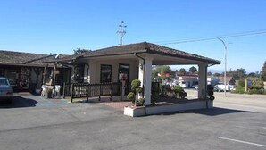 A building with a covered outdoor seating area, a car parked in front, and a clear blue sky. - Monterey Fairgrounds Inn (Monterey)