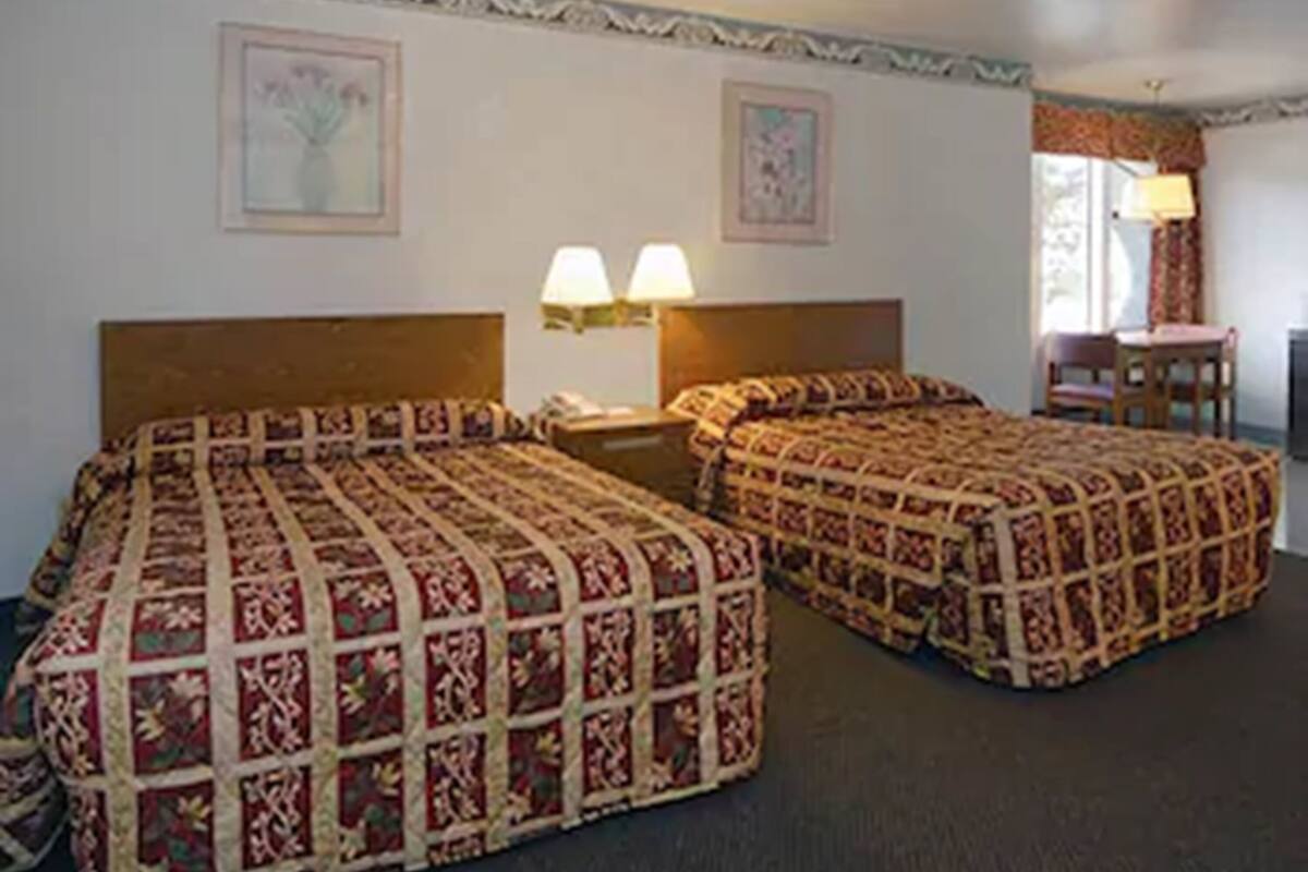 A hotel room with two beds, a desk, and a chair.