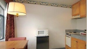 A compact kitchen with a refrigerator, microwave, stove, and a dining table with chairs. - Monterey Fairgrounds Inn (Monterey)