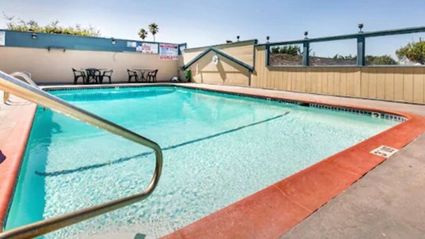 A swimming pool with a metal ladder, surrounded by a beige wall and a blue sky. - Monterey Fairgrounds Inn (Monterey)