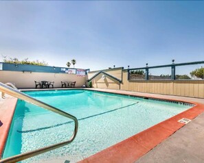 A swimming pool with a metal ladder, surrounded by a beige wall and a blue sky. - Monterey Fairgrounds Inn (Monterey)