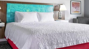 A hotel room with a large bed, a headboard with a map design, a nightstand with a lamp, and a chair.