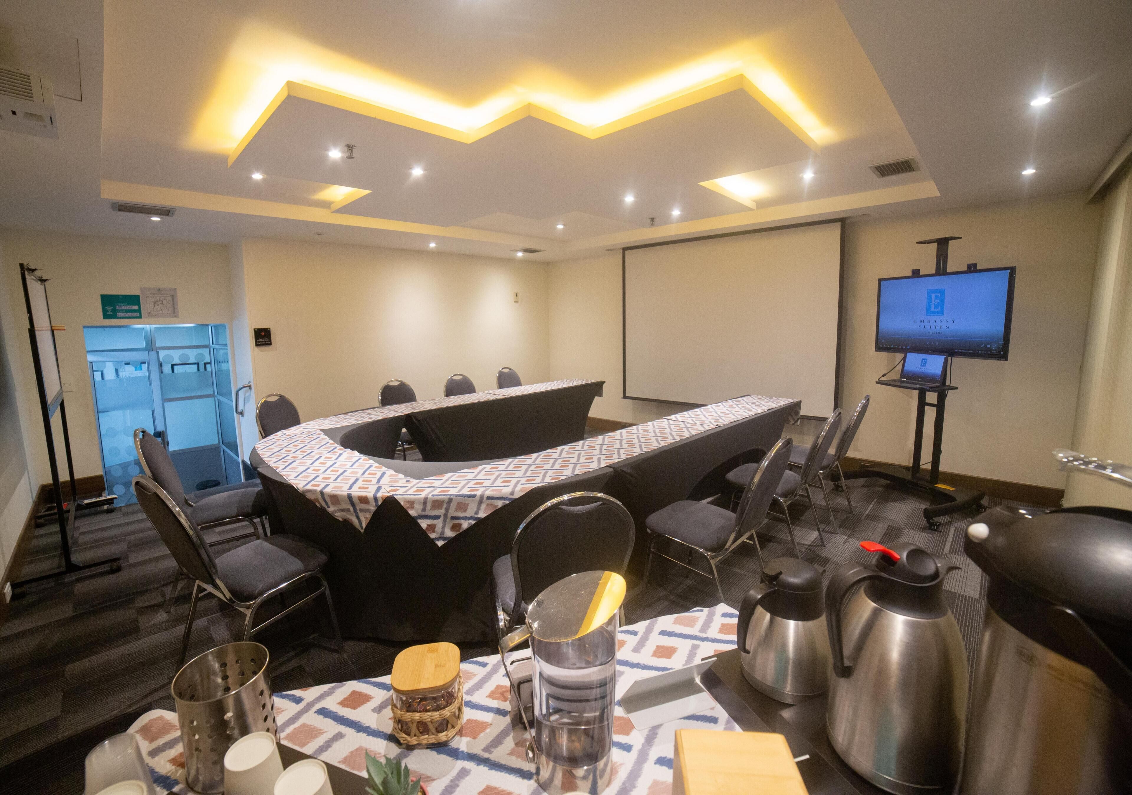 A conference room with a large table, chairs, a projector screen, and a television.