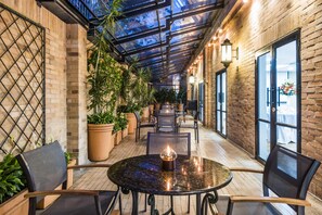 Een overdekt terras met bakstenen muren, potplanten en tafels met stoelen.