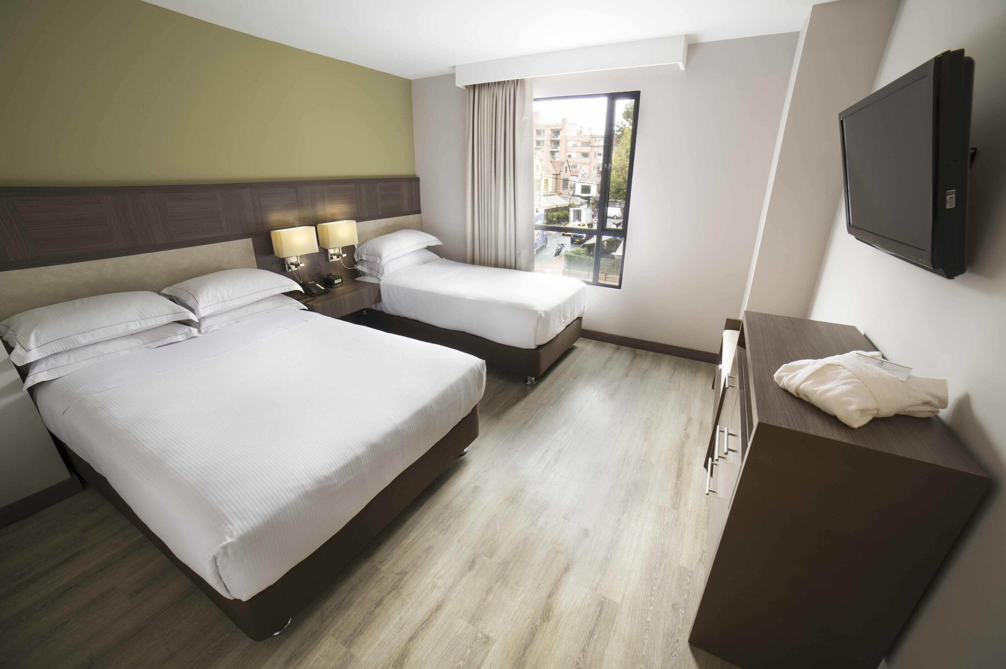 Une chambre d’hôtel avec deux lits, un bureau, une télévision et une fenêtre donnant sur des immeubles.