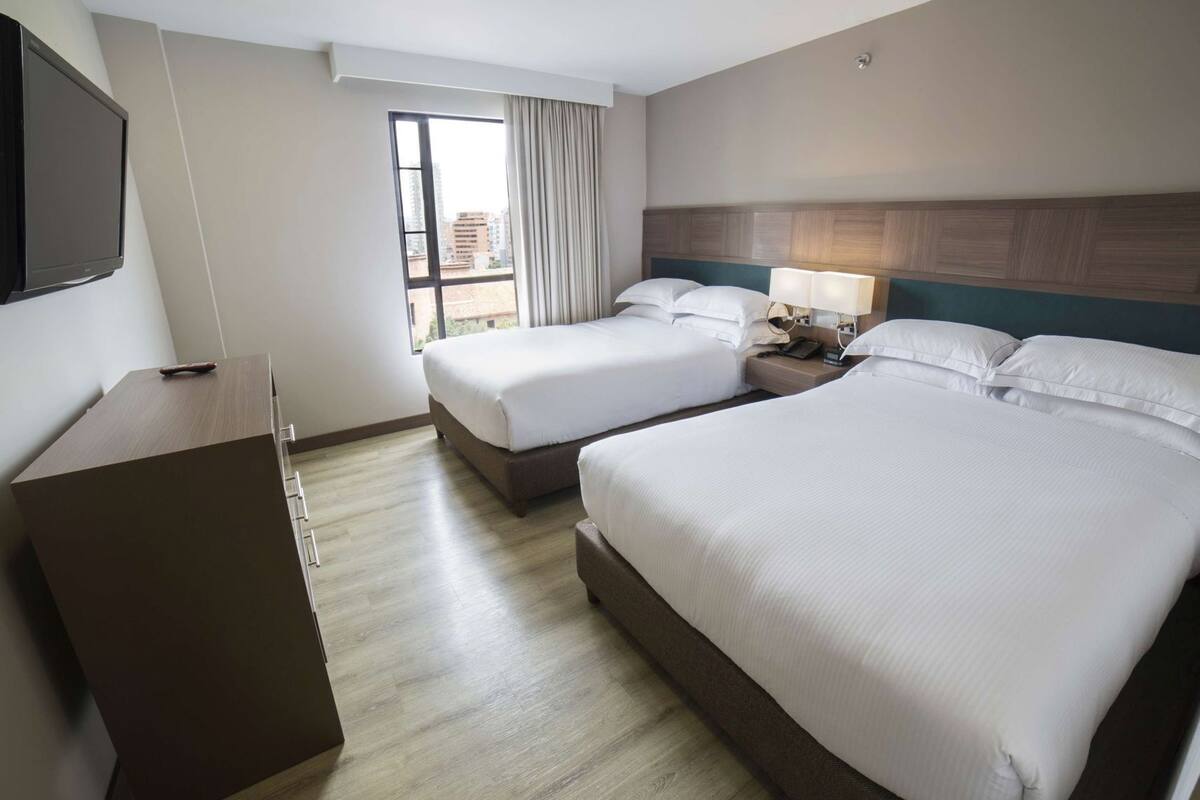 Ein Hotelzimmer mit zwei Betten, einem Fernseher, einem Schreibtisch und einem Fenster mit Vorhängen.