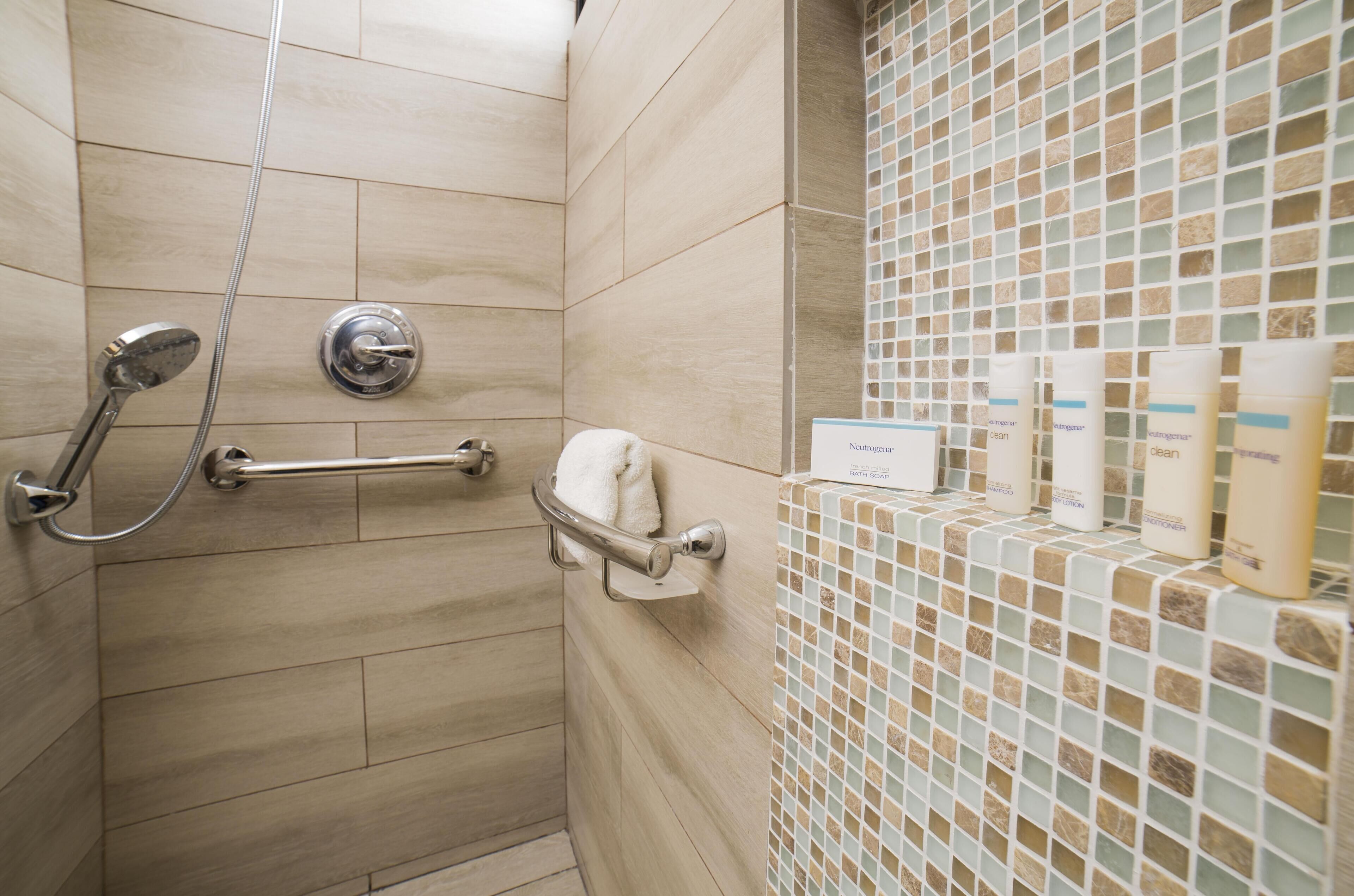 Ein Duschbereich mit Haltegriff, Handtuchhalter und einer gefliesten Wand mit Badezimmerartikeln.
