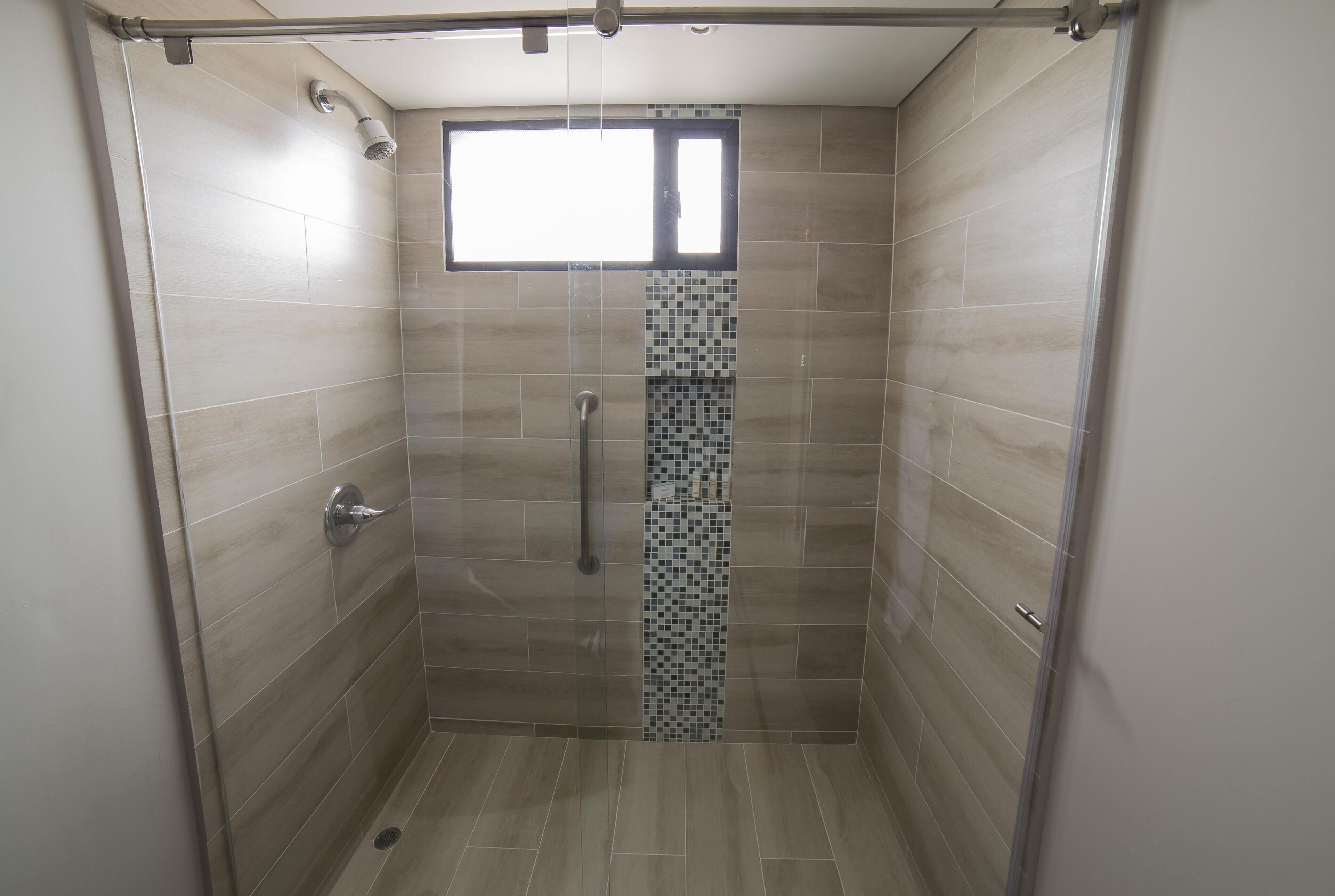 Une douche avec une fenêtre, des murs carrelés et un robinet en métal.