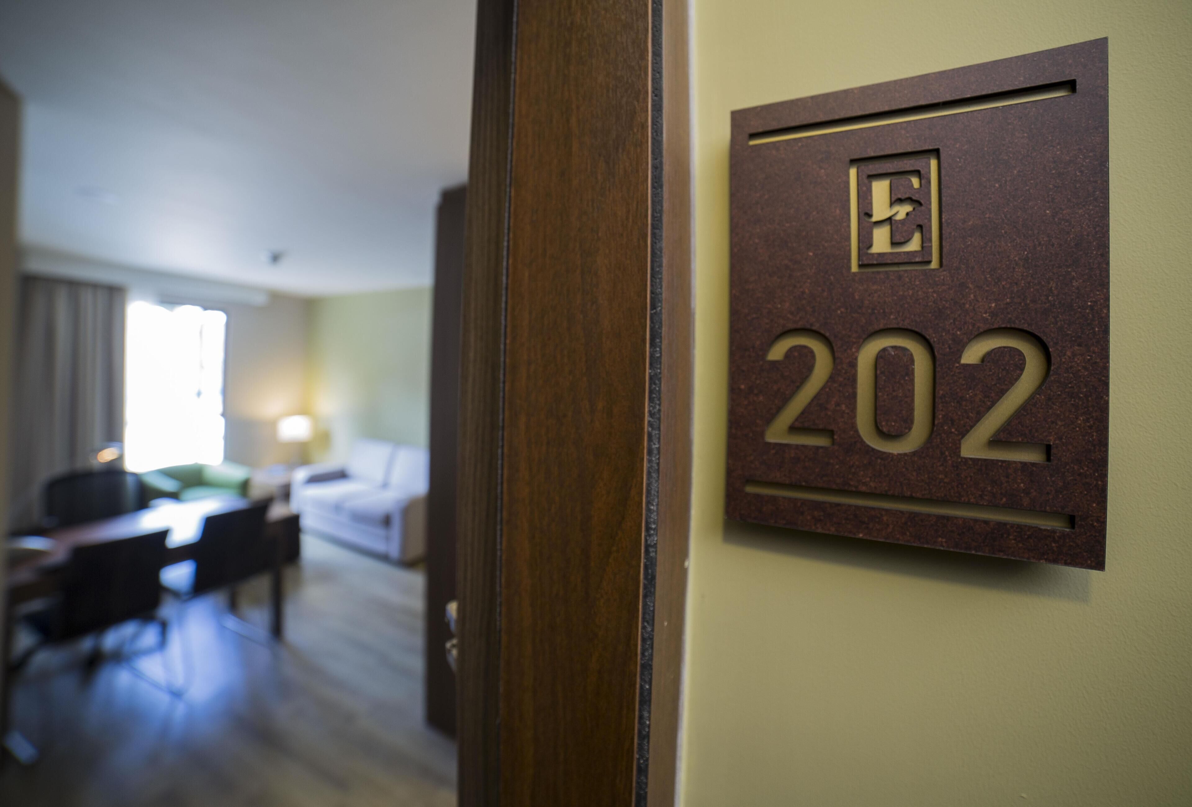 Habitación de hotel con una puerta que indica 'E 202' y una vista parcial de una cama y un escritorio al fondo.