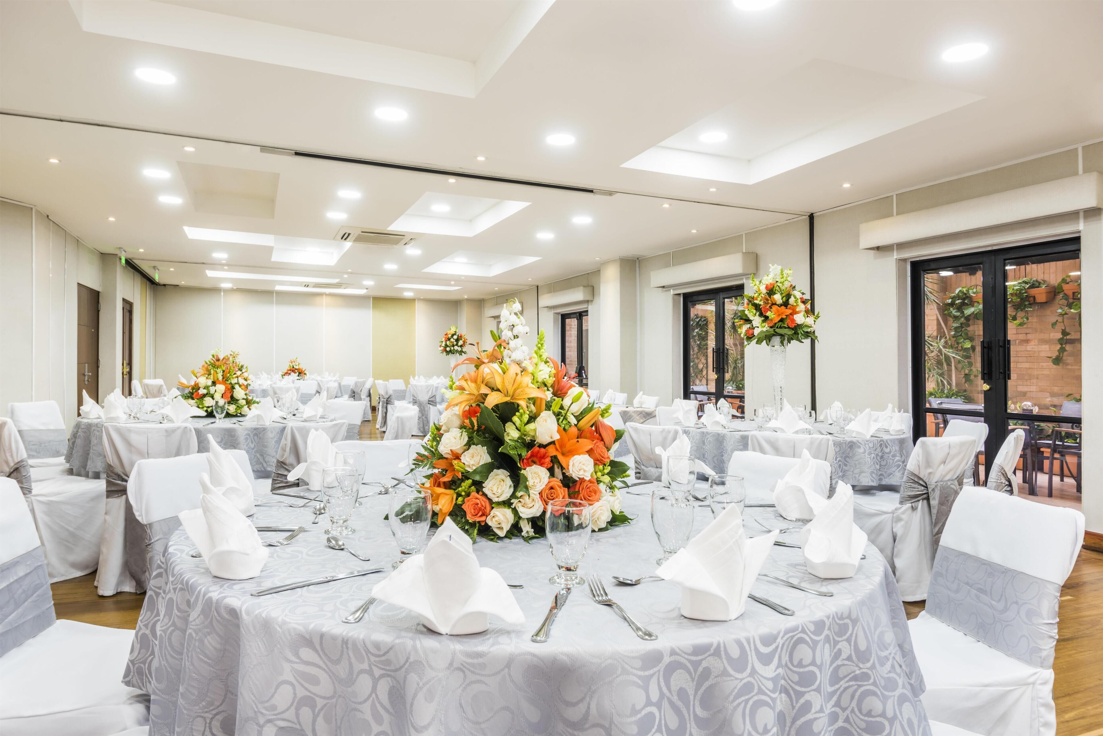 A banquet hall with round tables, white tablecloths, and floral centerpieces.