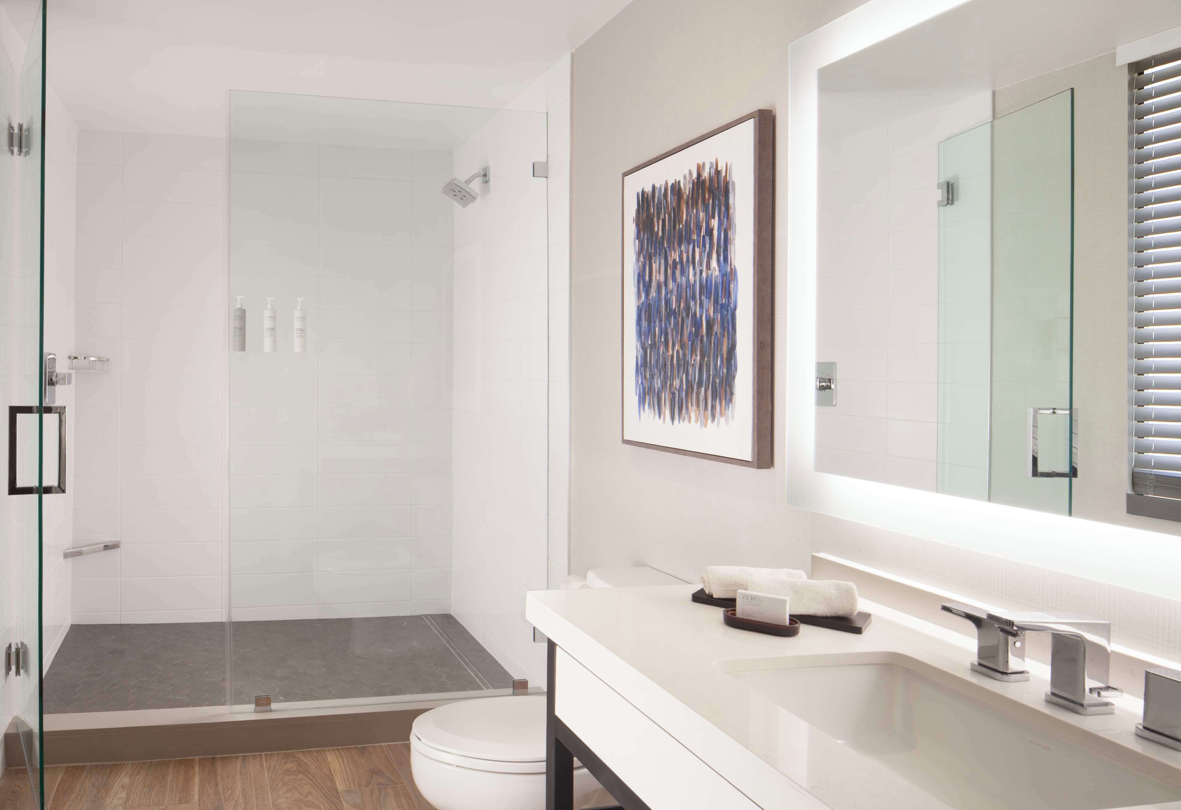 A modern bathroom with a glass shower enclosure, a large mirror, and a white vanity.