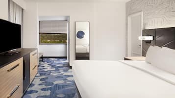 Quarto de hotel com cama, televisão, escrivaninha e janela com persianas.