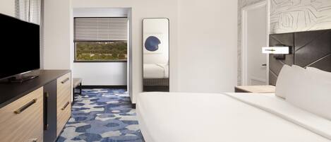 Une chambre d’hôtel avec un lit, une télévision, un bureau et une fenêtre avec des stores.