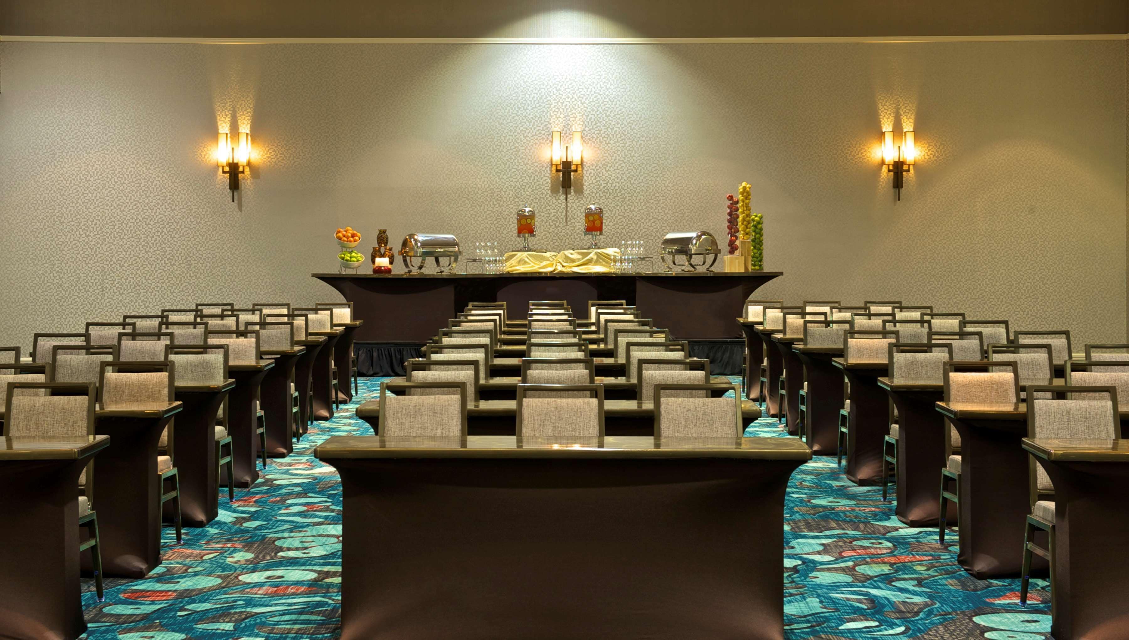 A conference room with rows of chairs, a long table, and wall sconces.