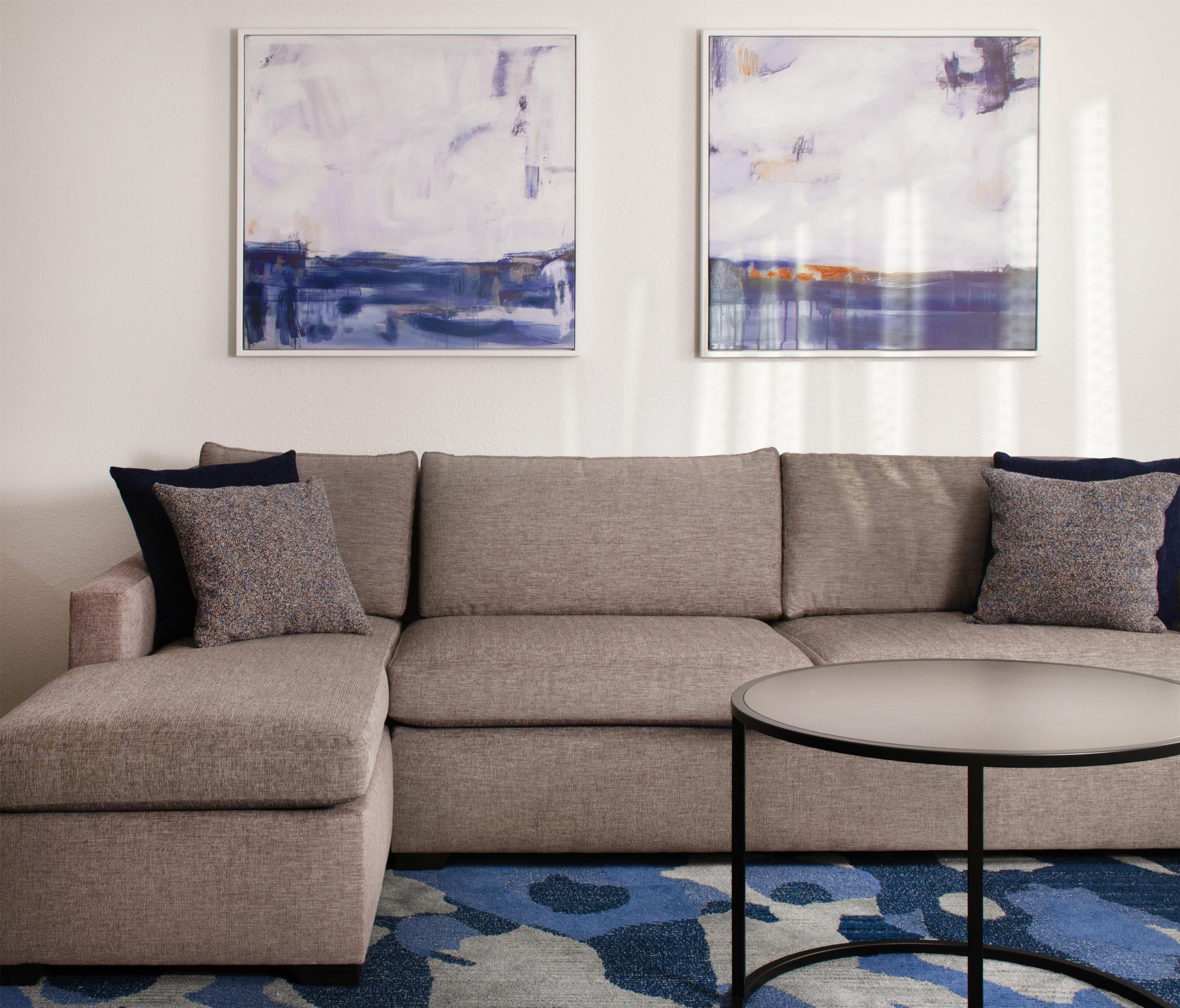 A sectional sofa with a round coffee table in a room with abstract paintings on the wall.