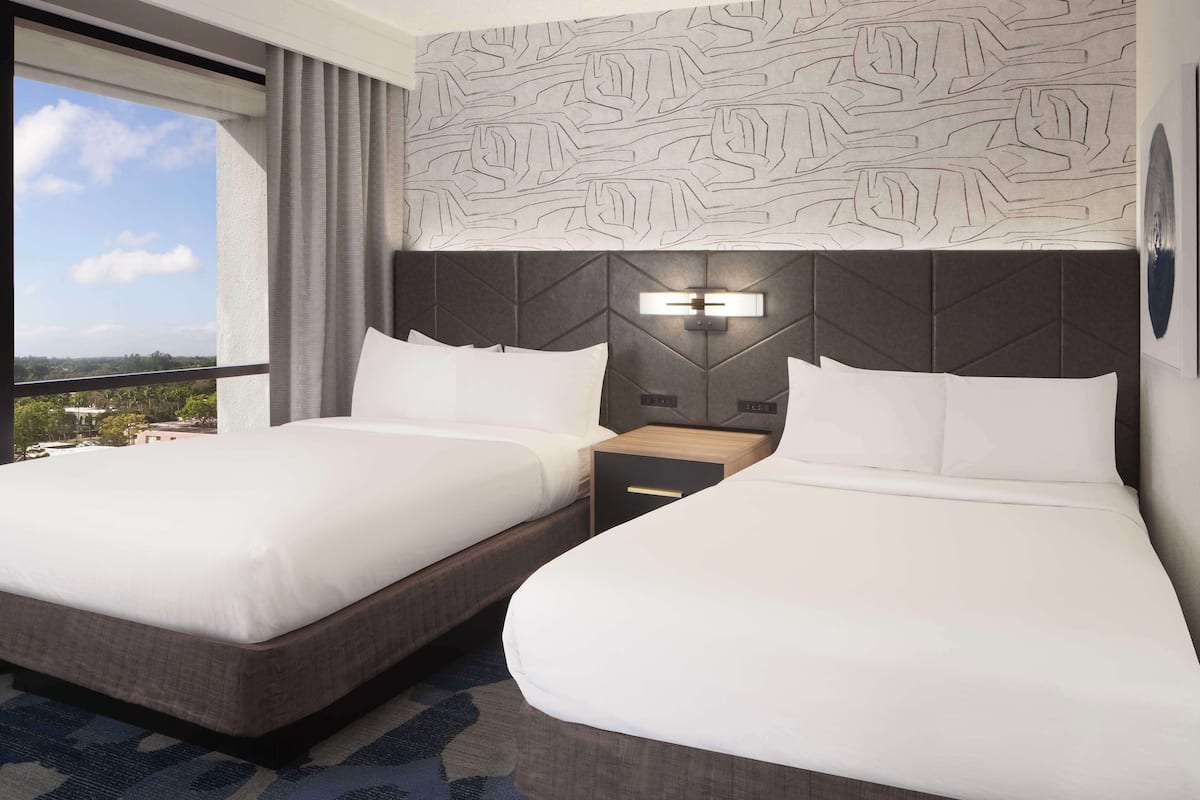 A hotel room with two beds, a large window, and a patterned wall.