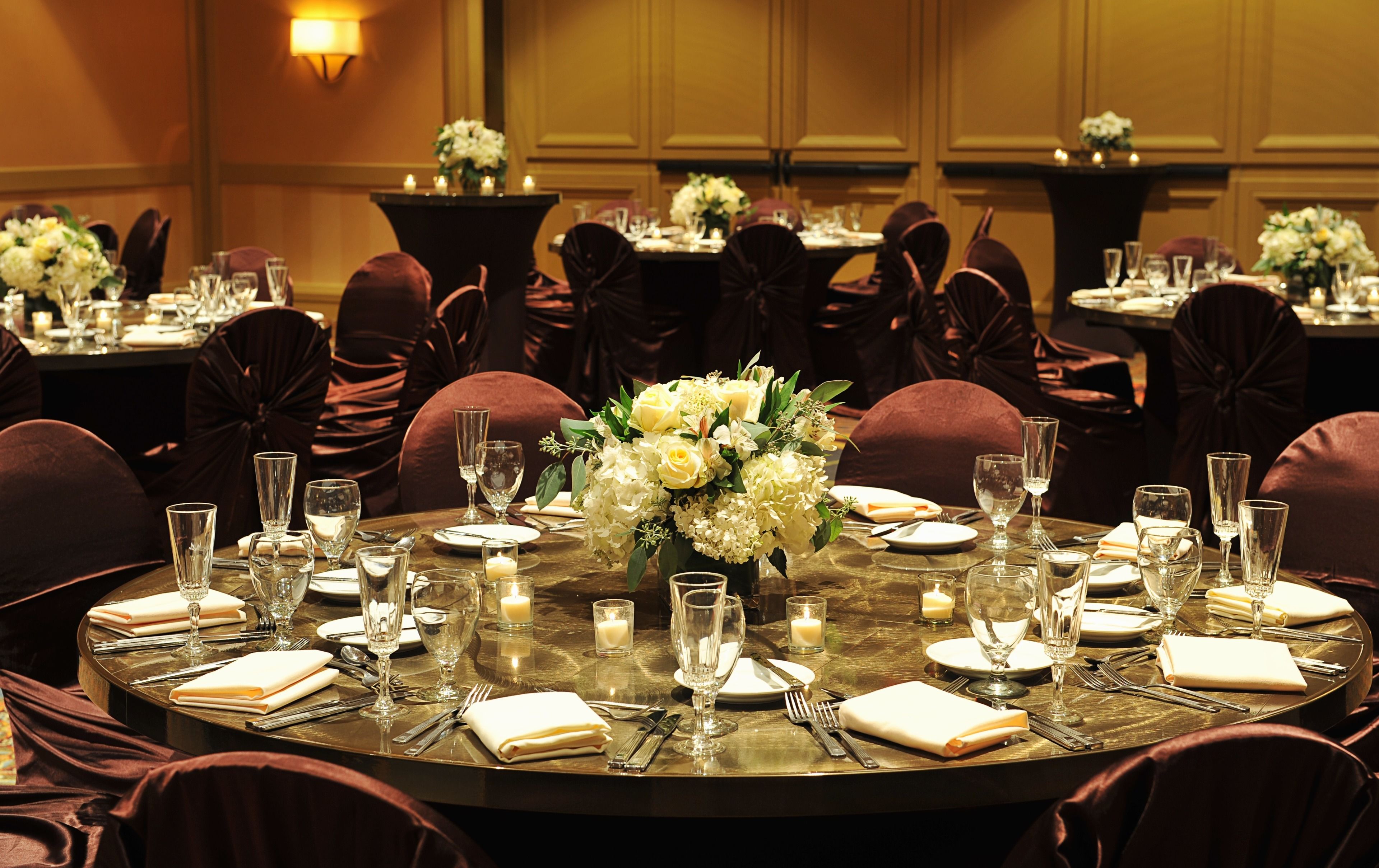 Une table ronde dressée pour un événement formel, avec des chaises, de la vaisselle et des centres de table floraux.