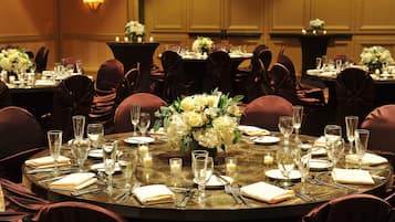 Une table ronde dressée pour un événement formel, avec des chaises, de la vaisselle et des centres de table floraux.