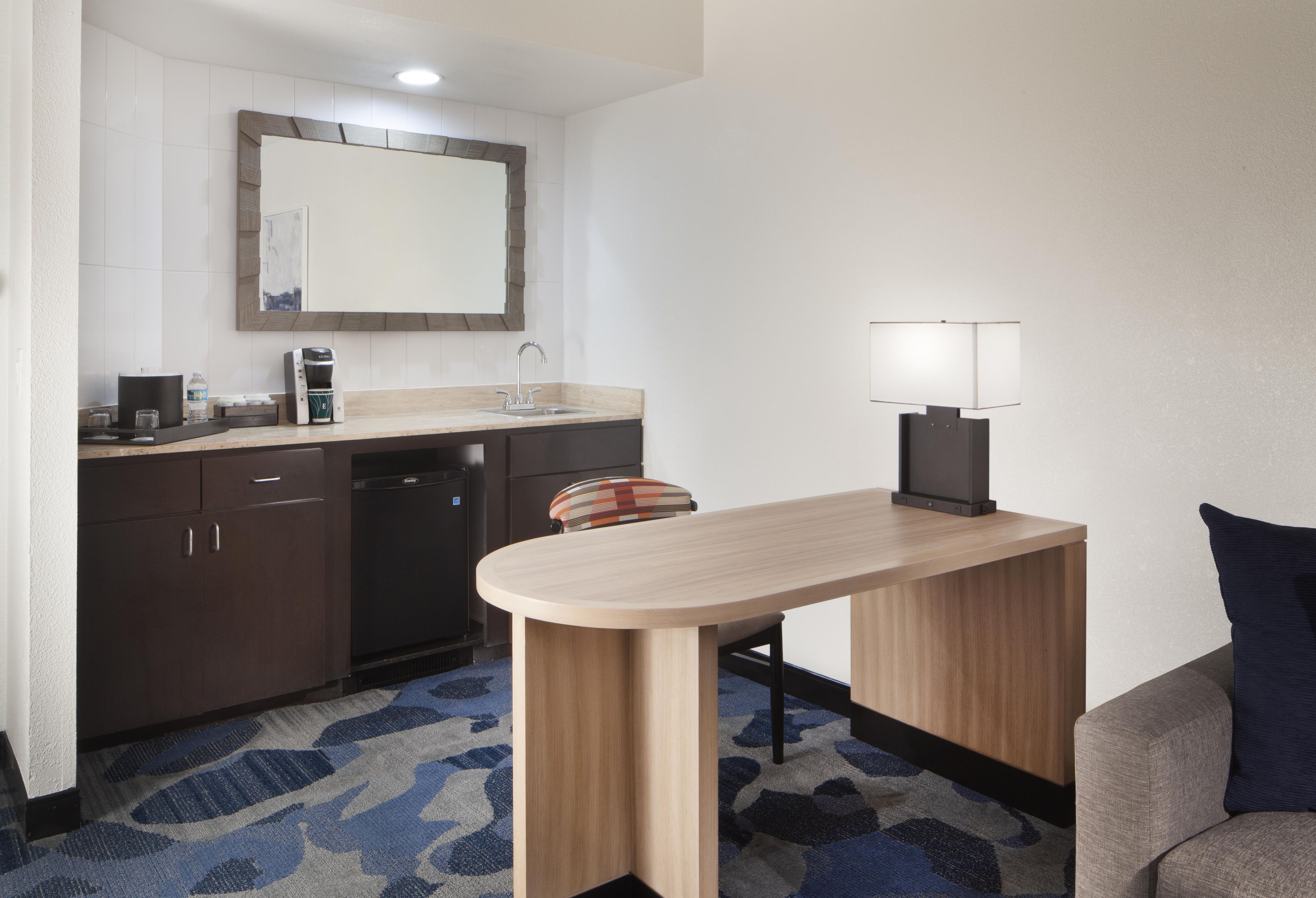 A compact hotel room with a kitchenette, a small dining table, a sofa, and a single bed.