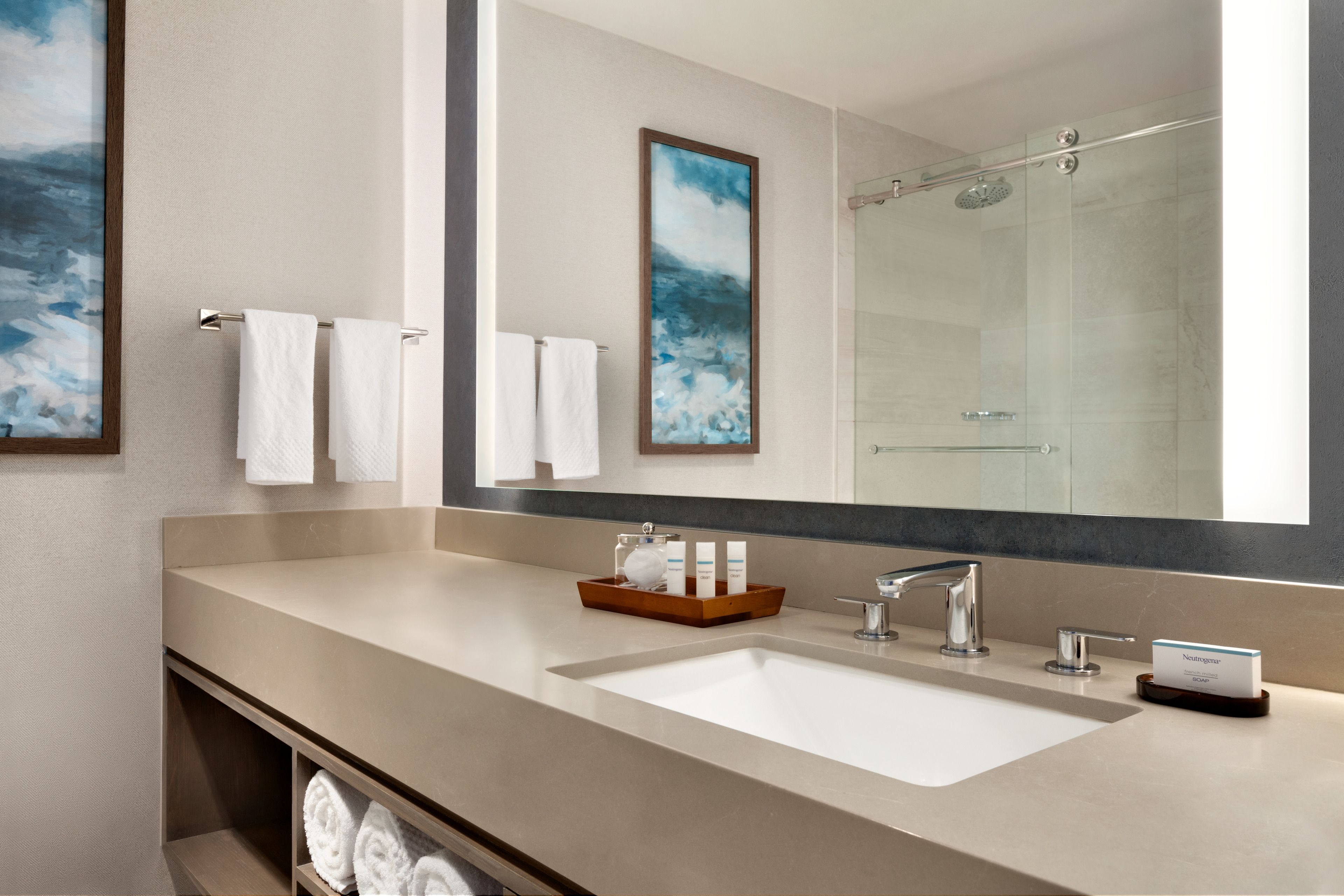 Un baño moderno con un espejo grande, un lavamanos y una ducha.