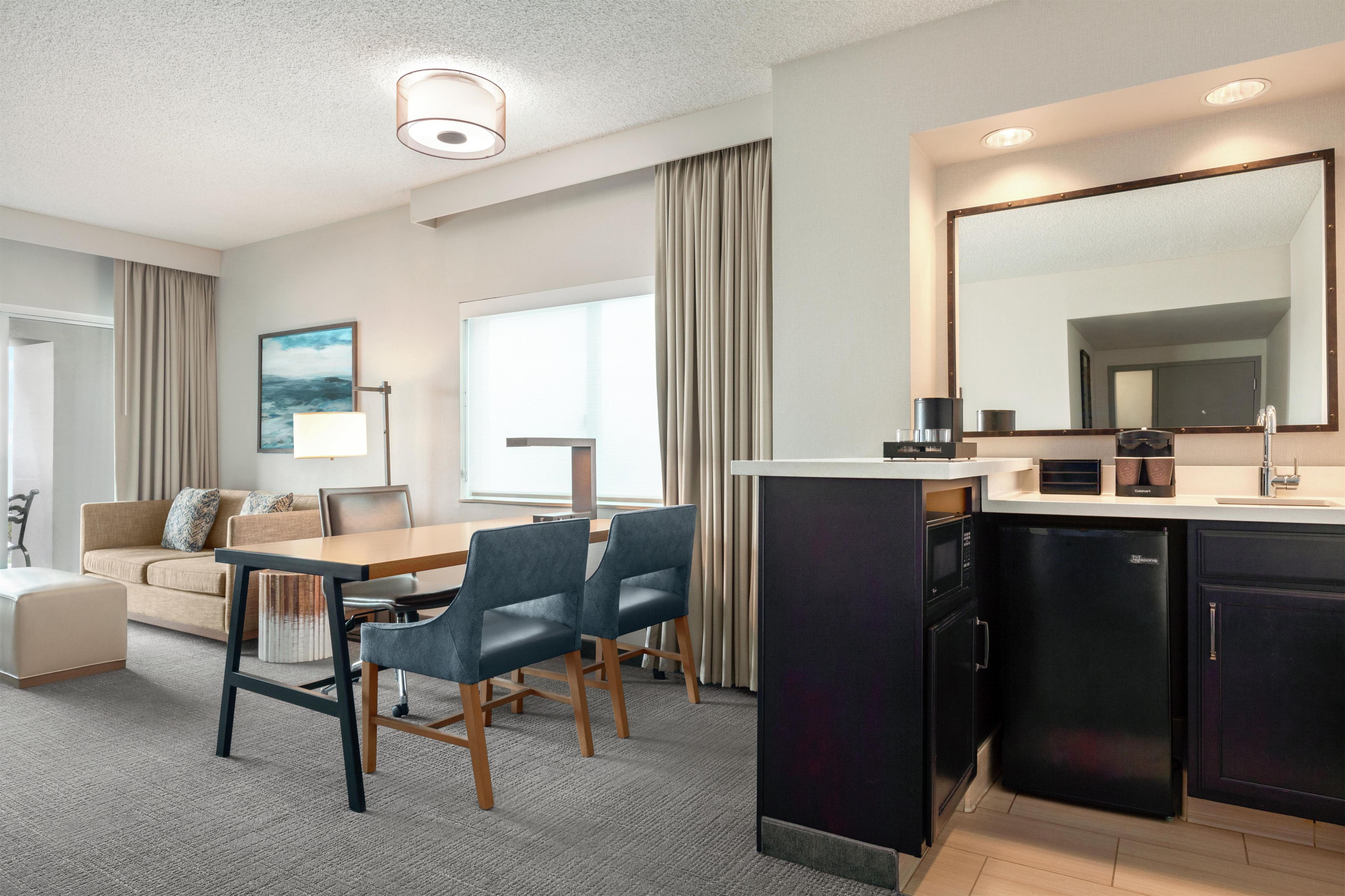 Een moderne hotelkamer met een zithoek, kitchenette en een groot raam.