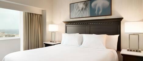 A hotel room with a large bed, two bedside tables, a window with curtains, and a wall-mounted artwork.