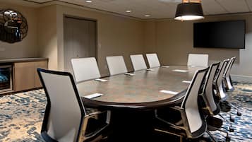 A conference room with a round table, white chairs, a flat-screen TV, and a ceiling light fixture.