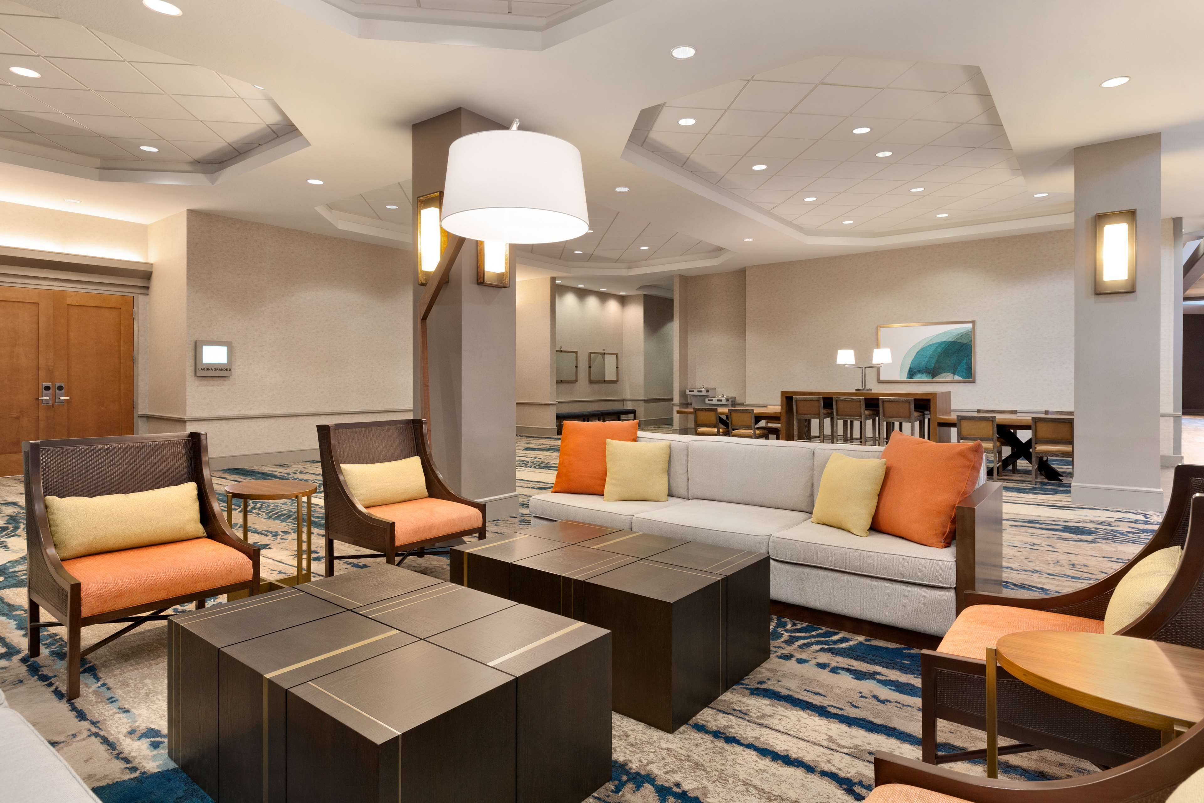 A spacious lobby with a sofa, chairs, and a coffee table. There is a reception desk and a large painting on the wall.