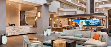 A spacious lobby with a reception desk, seating area, and a large TV screen.