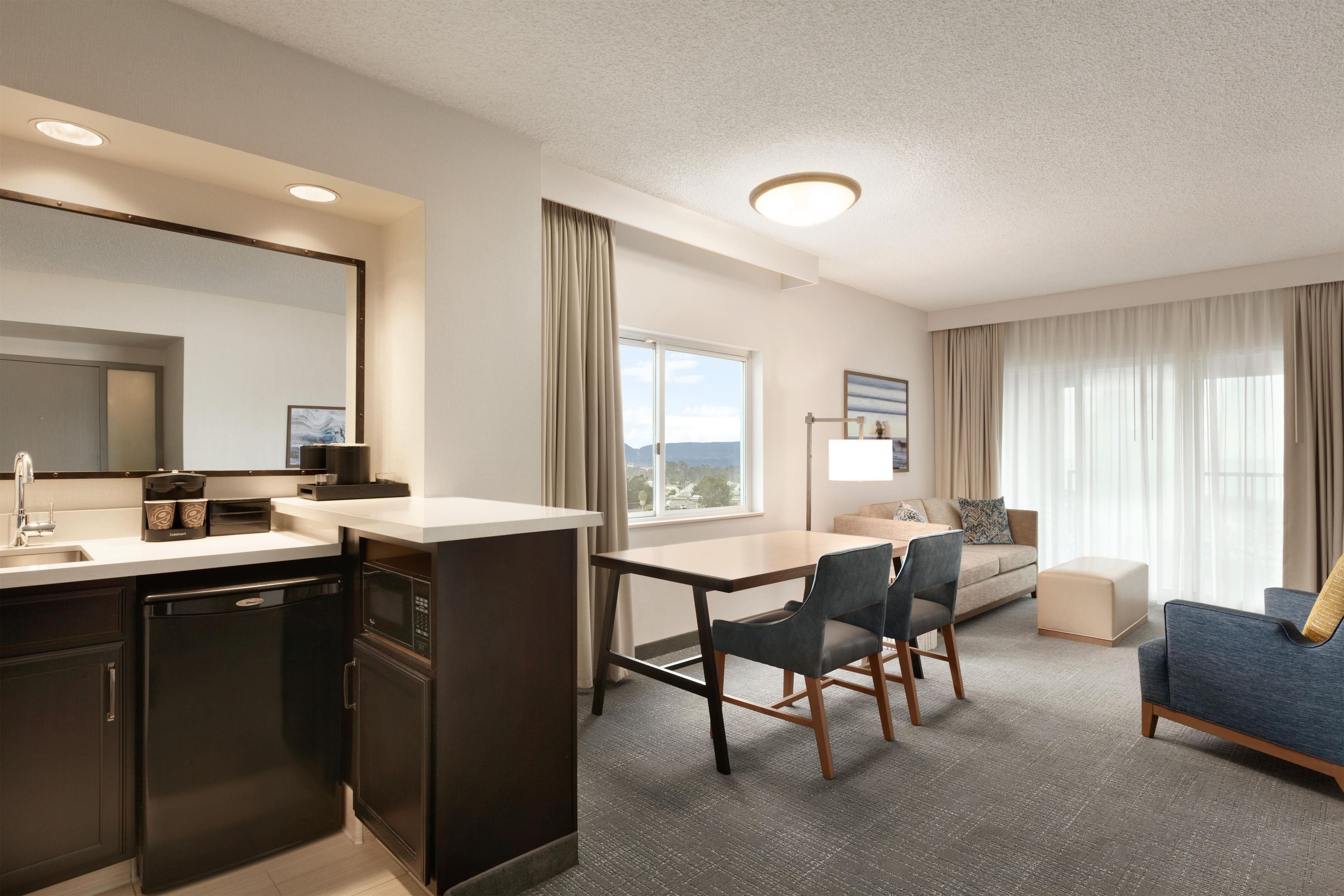 Ein modernes Hotelzimmer mit Küchenzeile, Essbereich, einer Couch und einem großen Fenster mit Blick.