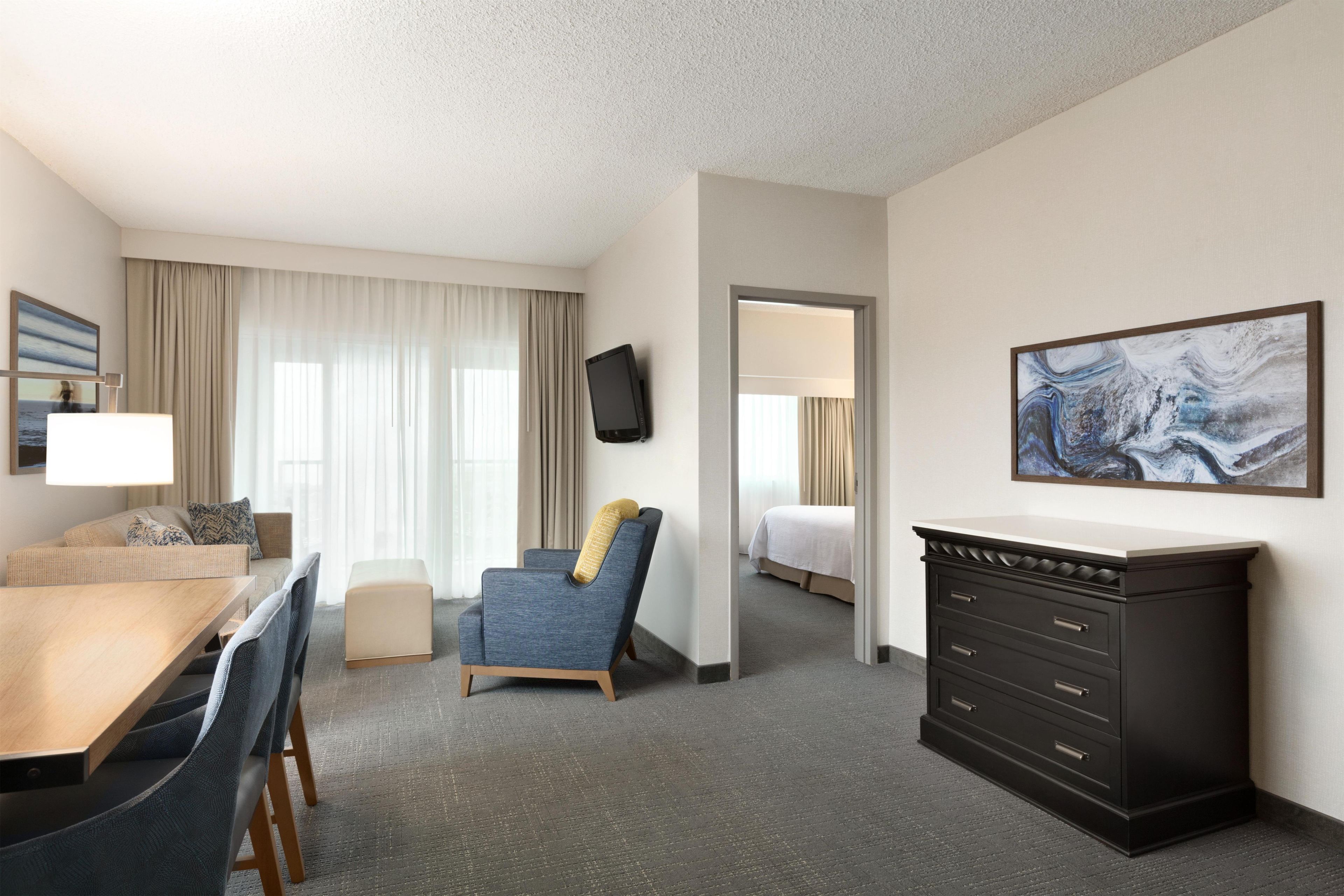 Une chambre d’hôtel avec un lit, un bureau, une chaise, une commode et un tableau au mur.