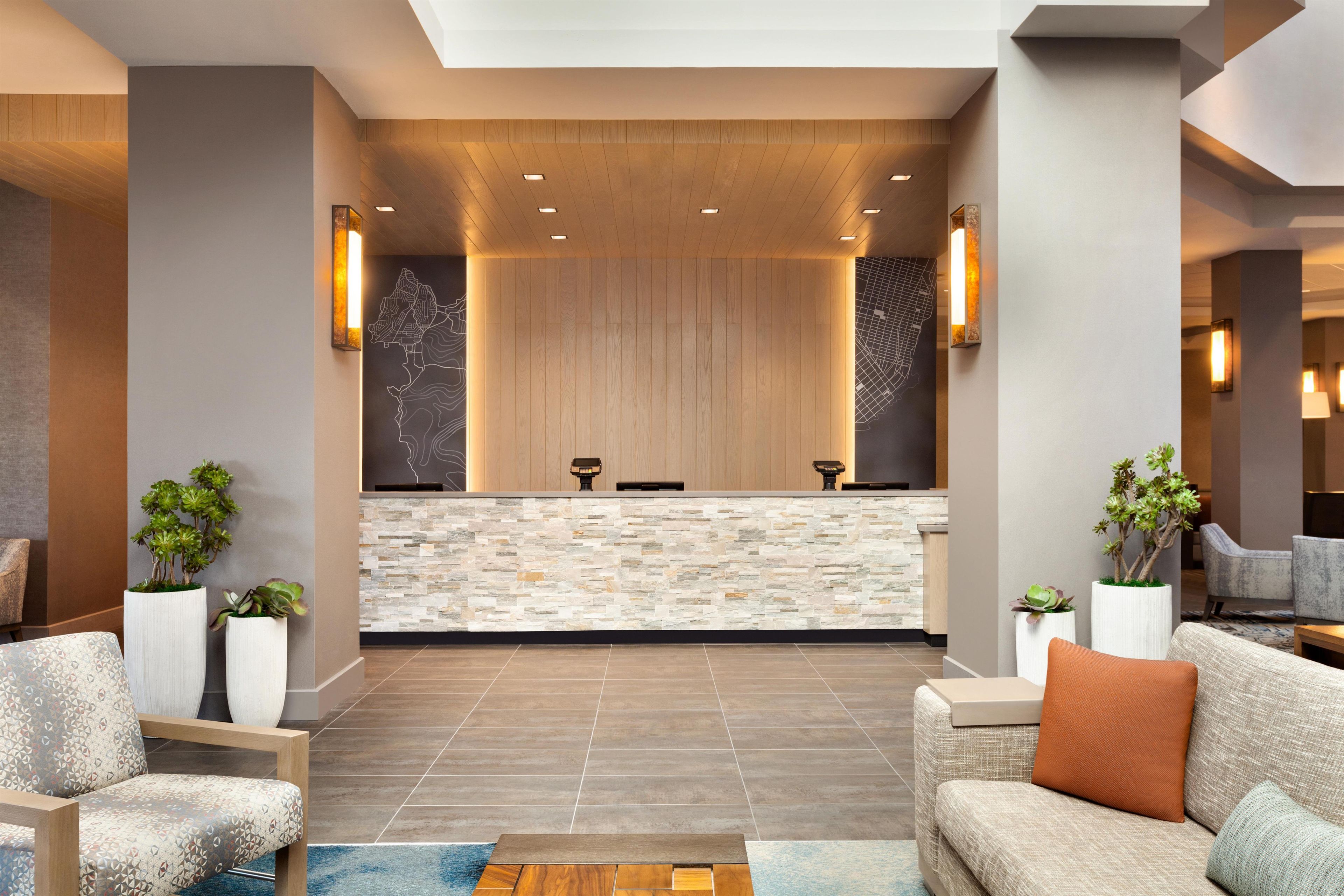 A reception area with a stone counter, two receptionists, and a seating area with sofas and potted plants.