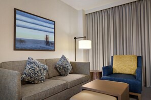 A hotel room with a sofa, a chair, a lamp, and a painting on the wall. - Embassy Suites by Hilton Monterey Bay Seaside (Seaside)