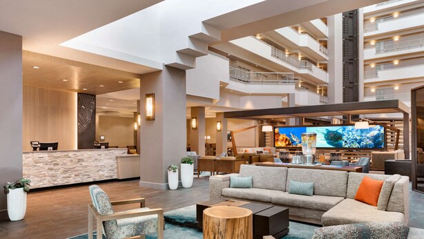 A modern hotel lobby with a reception desk, seating area, and a large TV screen. - Embassy Suites by Hilton Monterey Bay Seaside (Seaside)