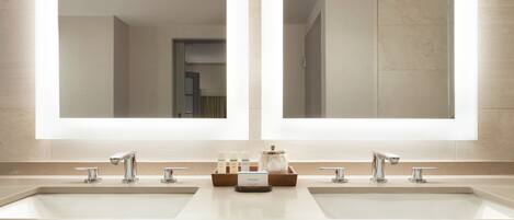 Un baño moderno con dos lavamanos, espejos grandes y un mueble de tocador con artículos de aseo.