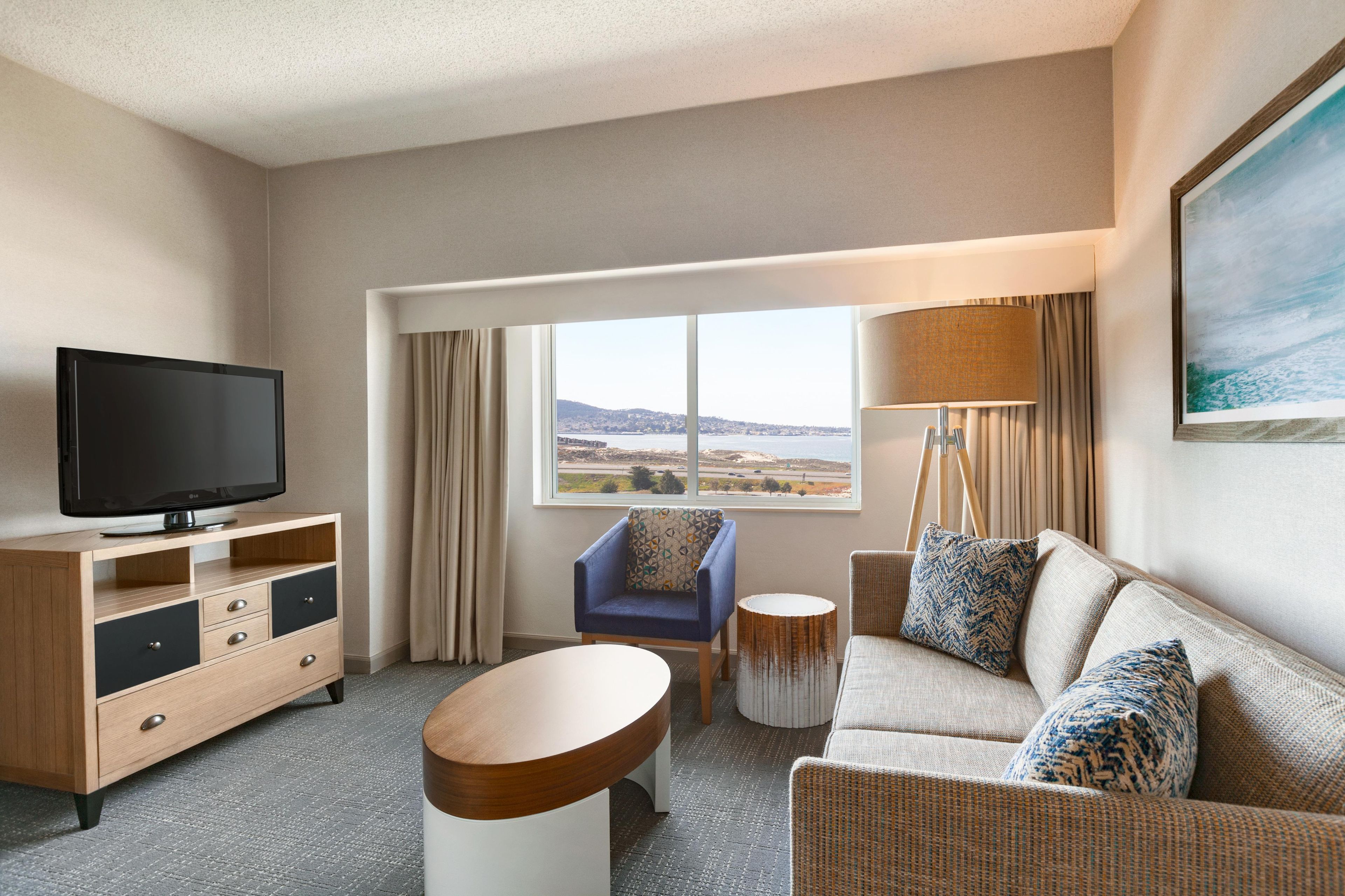 Een hotelkamer met een flatscreen televisie, een bank, een stoel, een klein tafeltje en een groot raam met uitzicht op het landschap.