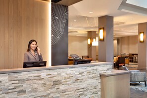 A reception desk with a stone wall, a digital kiosk, and a seating area with chairs and tables. - Embassy Suites by Hilton Monterey Bay Seaside (Seaside)
