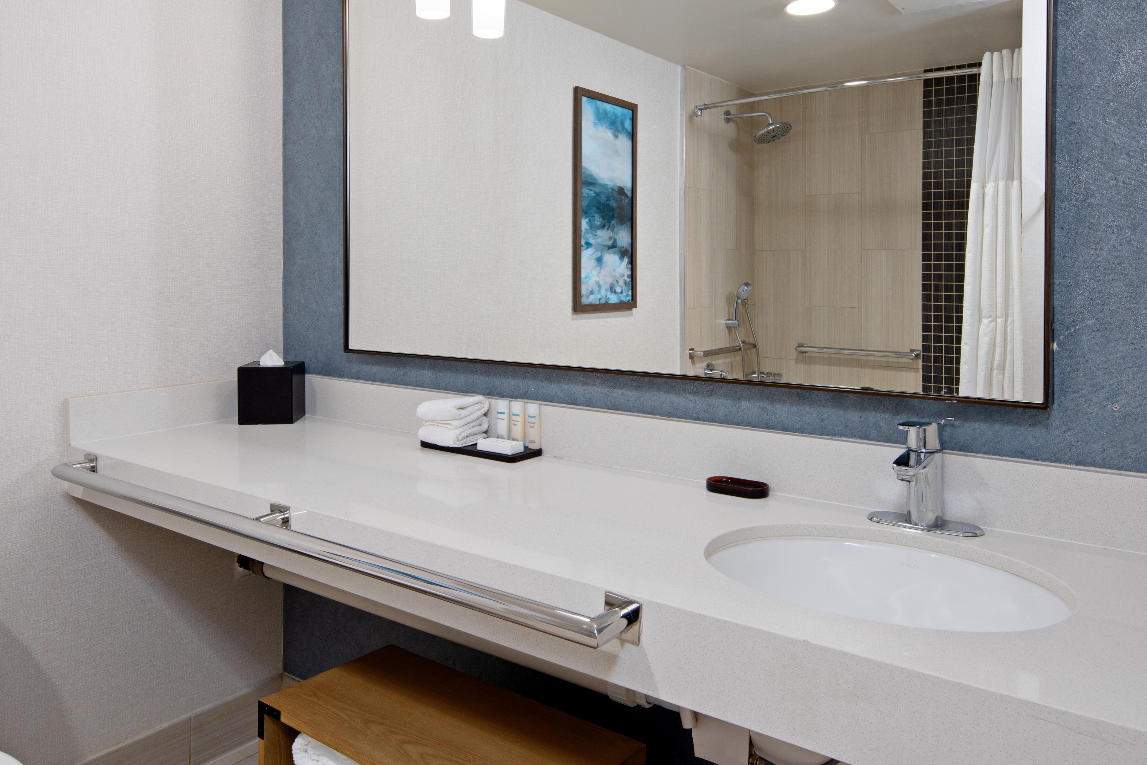 A bathroom with a white sink, a mirror, a towel rack, and a shower area.