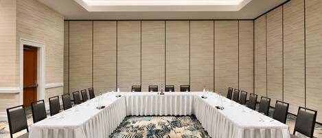 Un salón de conferencias con una mesa larga, sillas y una alfombra estampada.