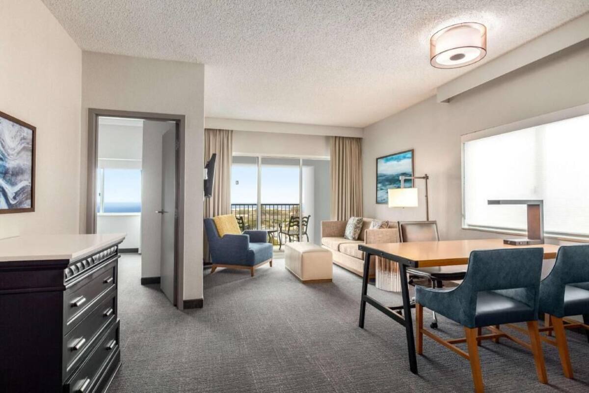 A hotel room with a balcony, a dining area, and a seating area with a view.