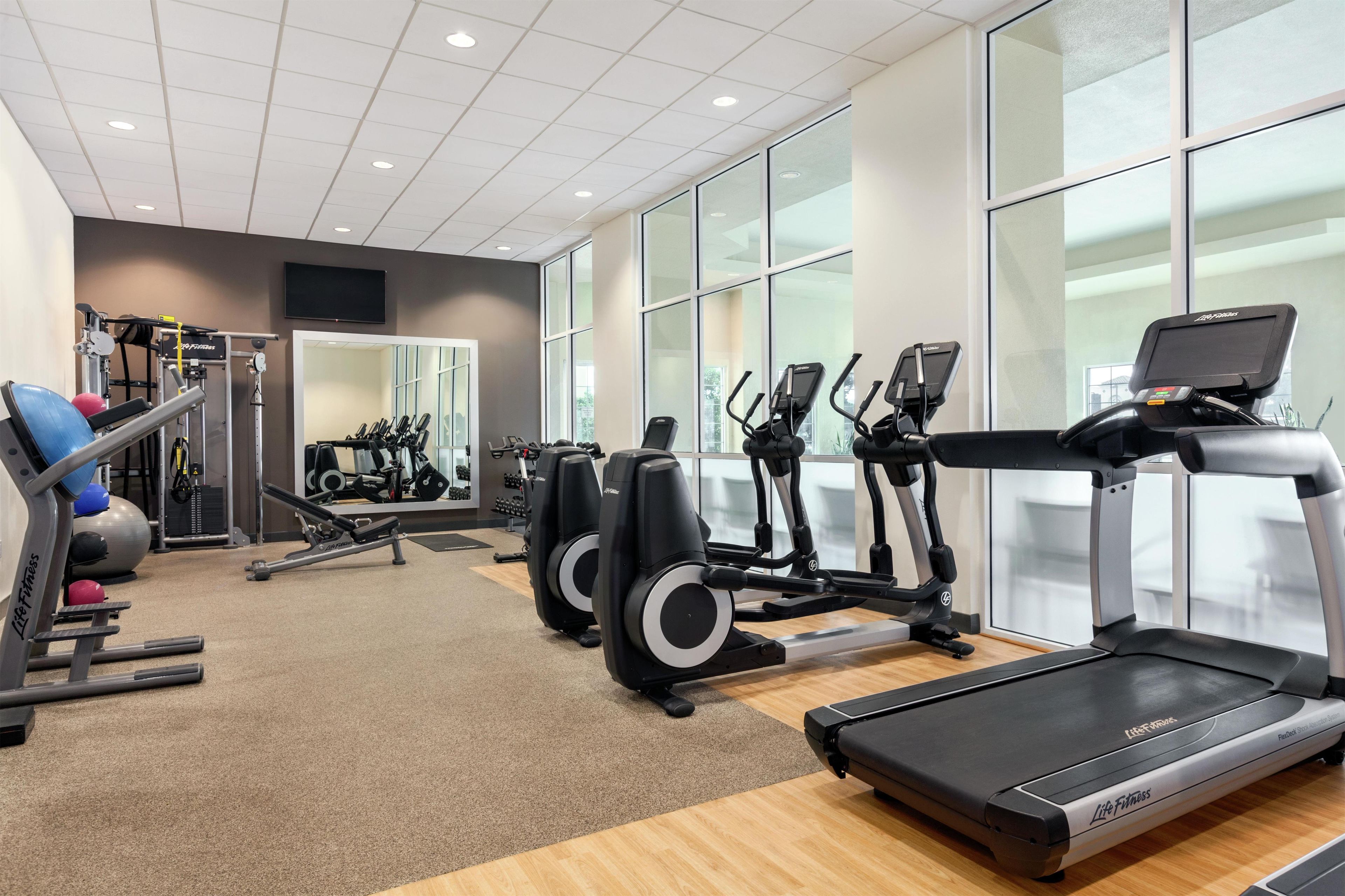 Un gimnasio con máquinas de cardio, equipo de levantamiento de pesas y un espejo grande.