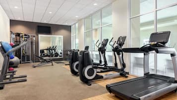 Un gimnasio con máquinas de cardio, equipo de levantamiento de pesas y un espejo grande.