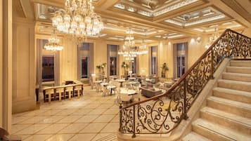 A grand lobby with a marble floor, ornate chandeliers, and a grand staircase.