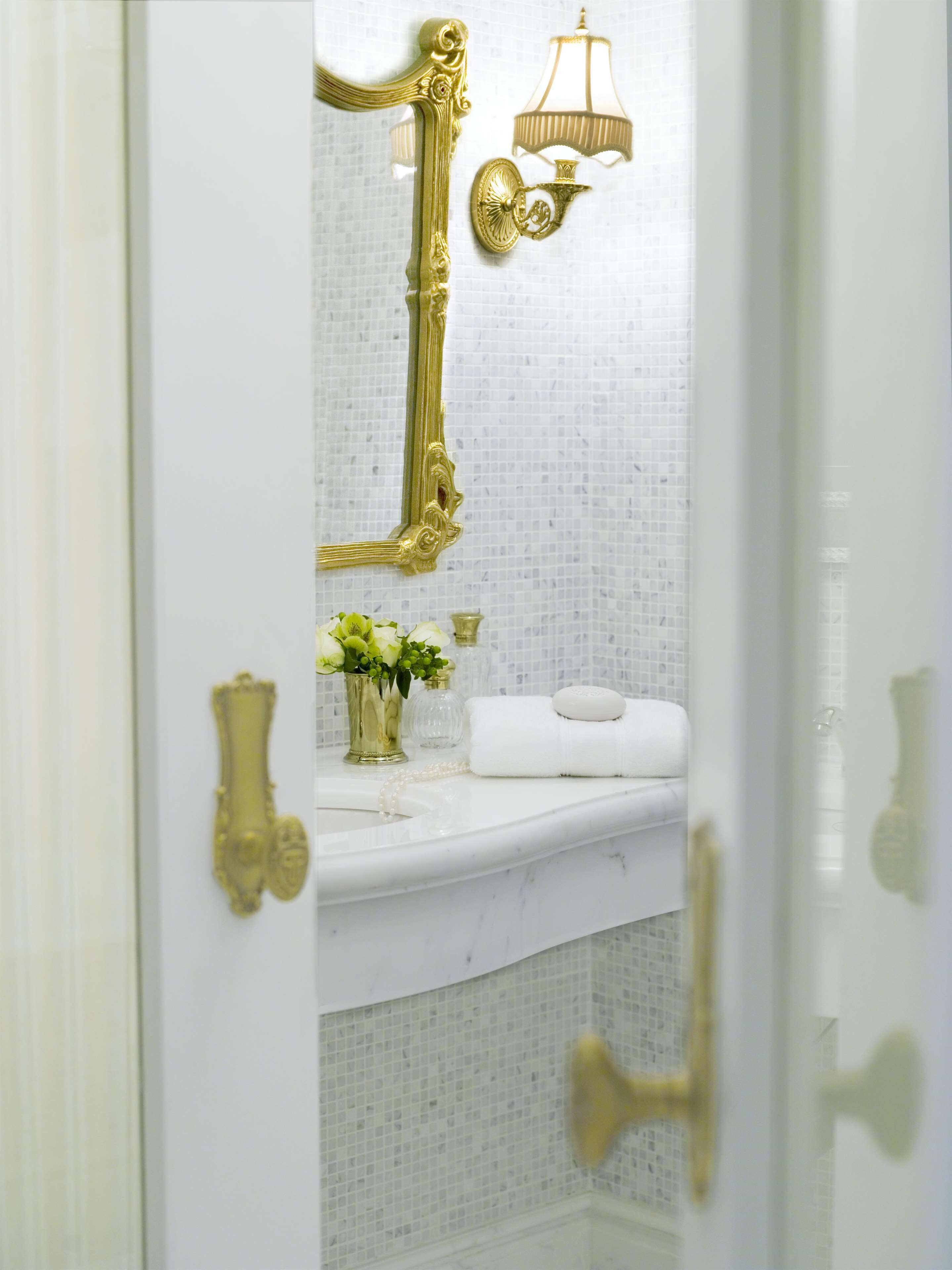 A bathroom with a white marble sink, gold fixtures, and a mirror with a gold frame.