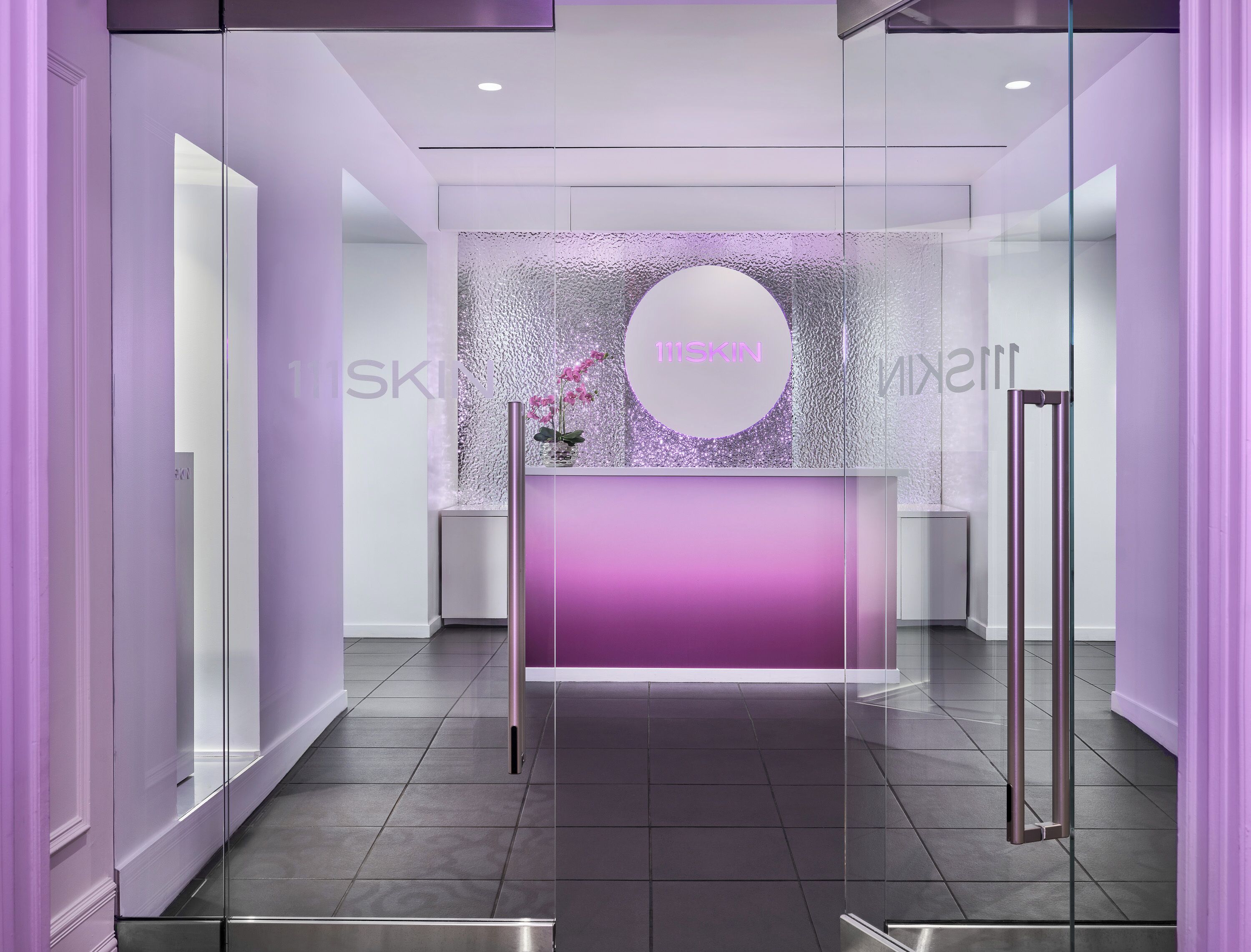 A reception area with a purple-lit counter, a decorative wall, and a glass door.