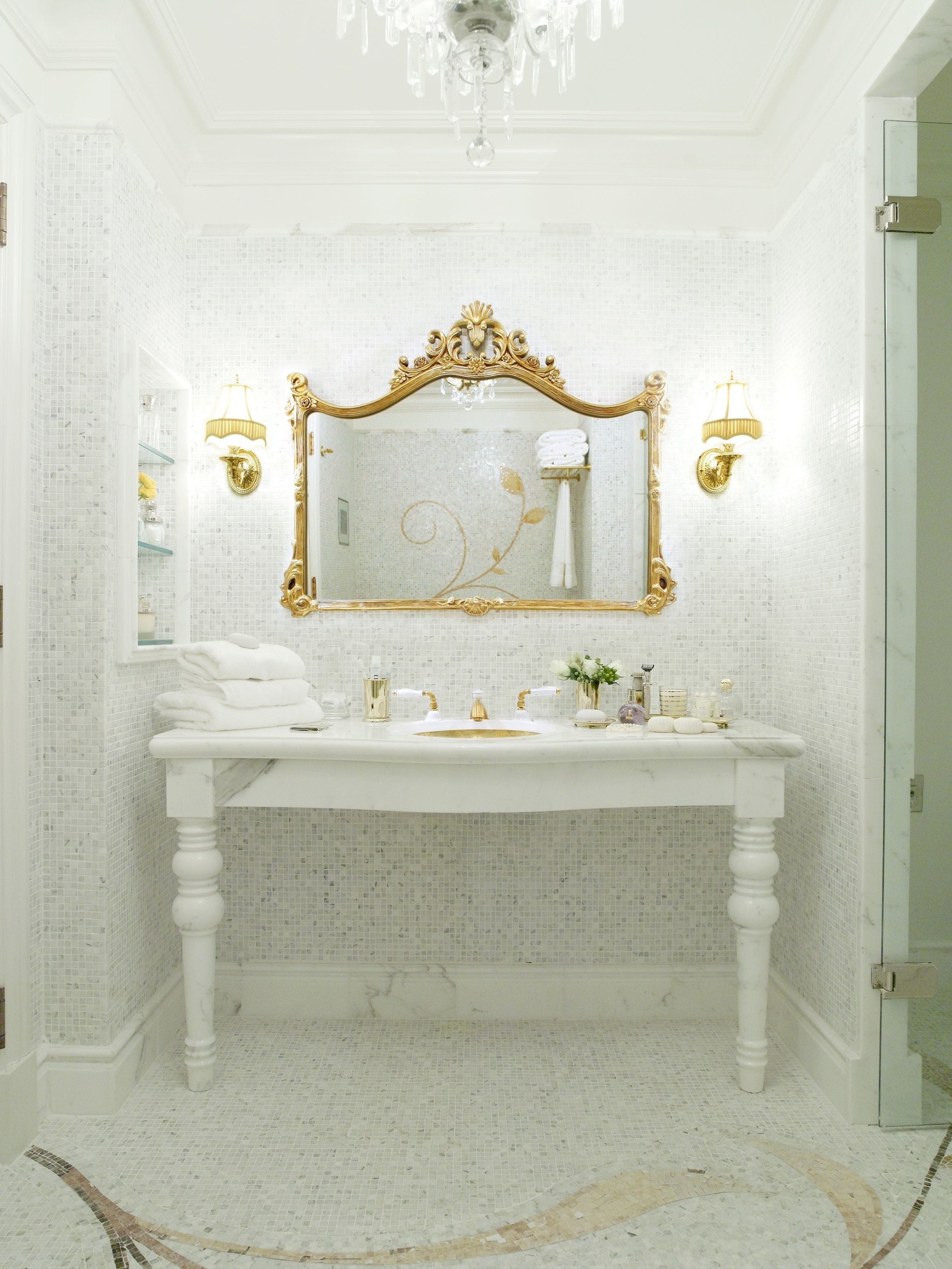 A bathroom with a white vanity, gold-framed mirror, and two wall-mounted lamps.
