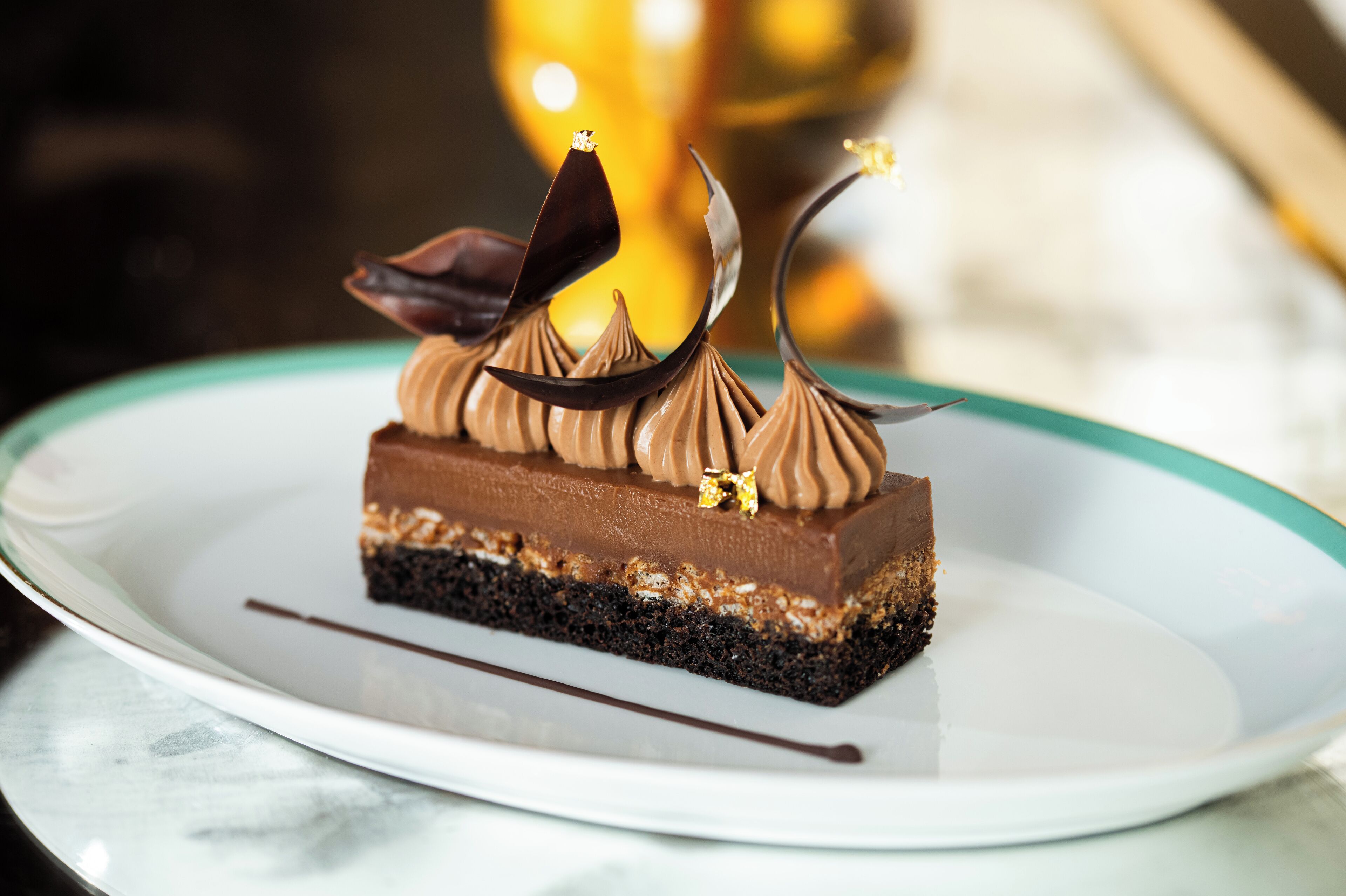 Une part de gâteau au chocolat, décorée de feuilles de chocolat, sur une assiette blanche.